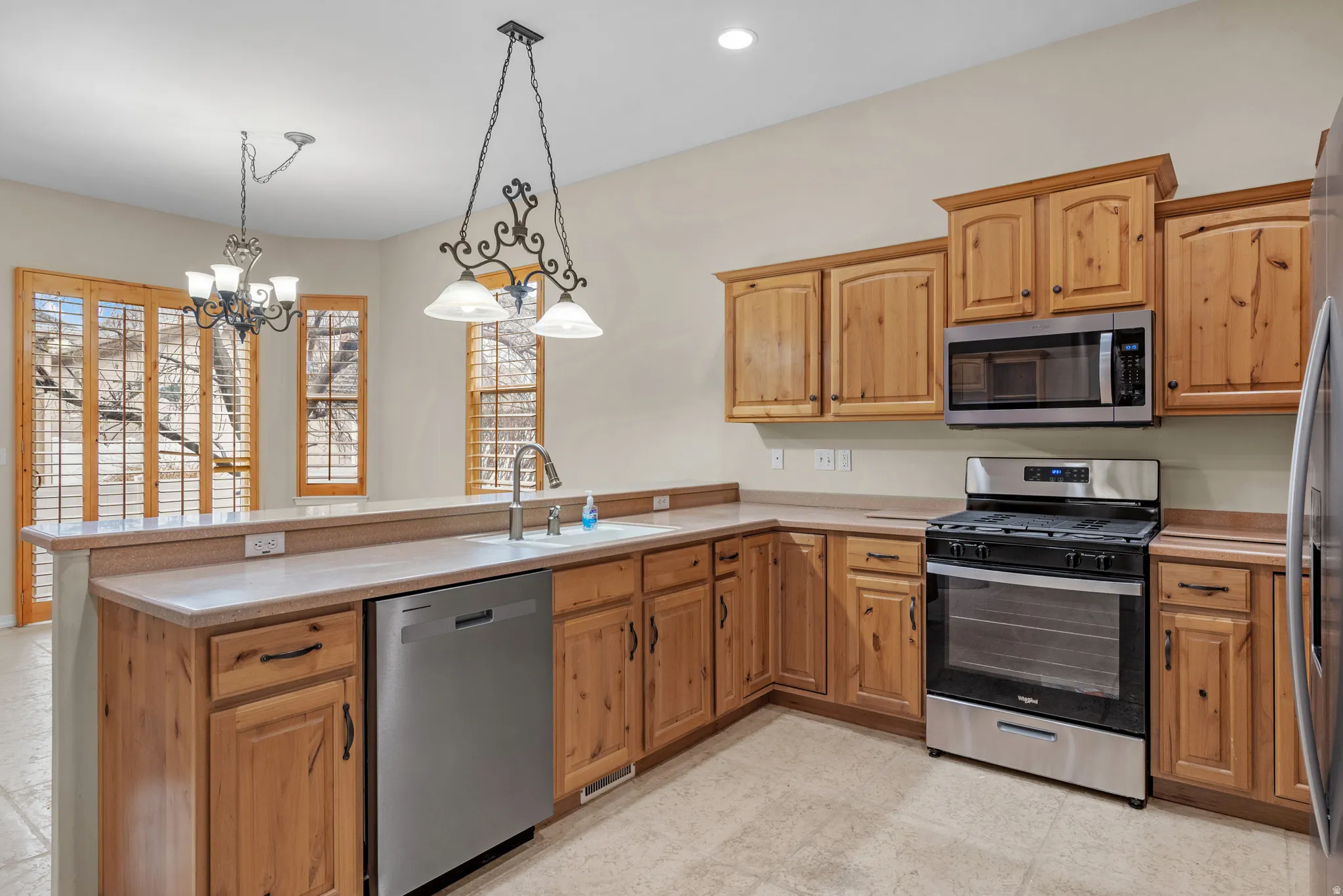 Kitchen featuring wood cabinetry, stainless steel appliances, a bar-height countertop, a stainless steel sink with a gooseneck faucet, and tile flooring