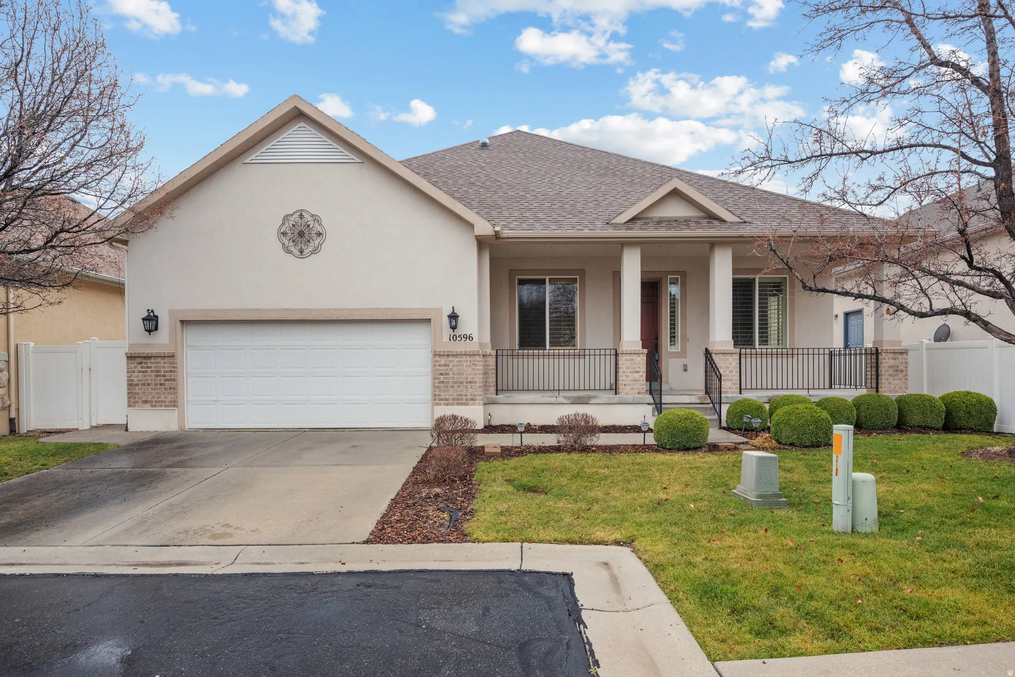 Stucco exterior with brick-finish accents, a covered front porch with pillars and iron railing, an attached garage, and a manicured lawn
