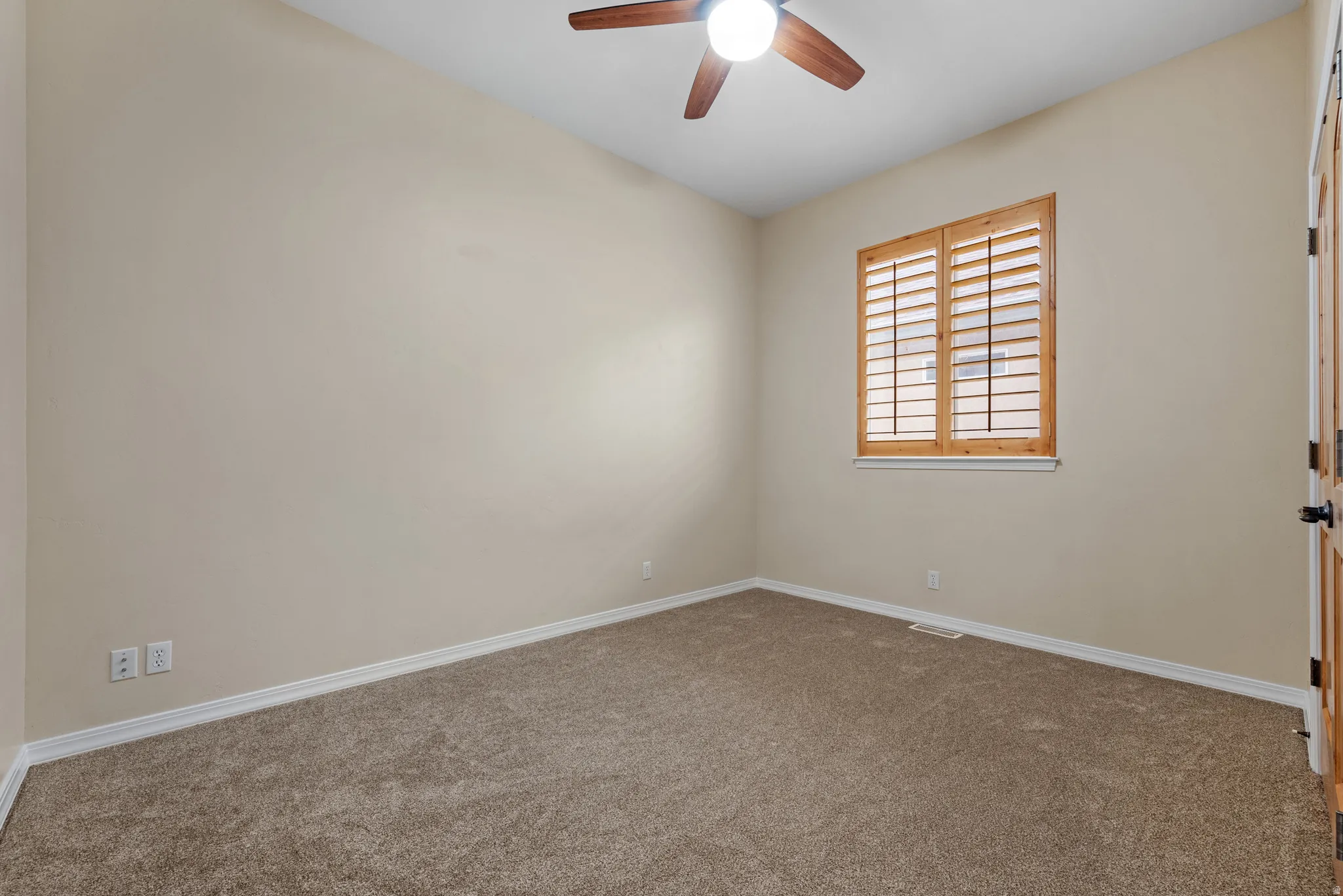 Bedroom featuring wood-finish plantation shutters, wood-finish ceiling fan with integrated lighting, neutral wall paint, and textured carpet flooring