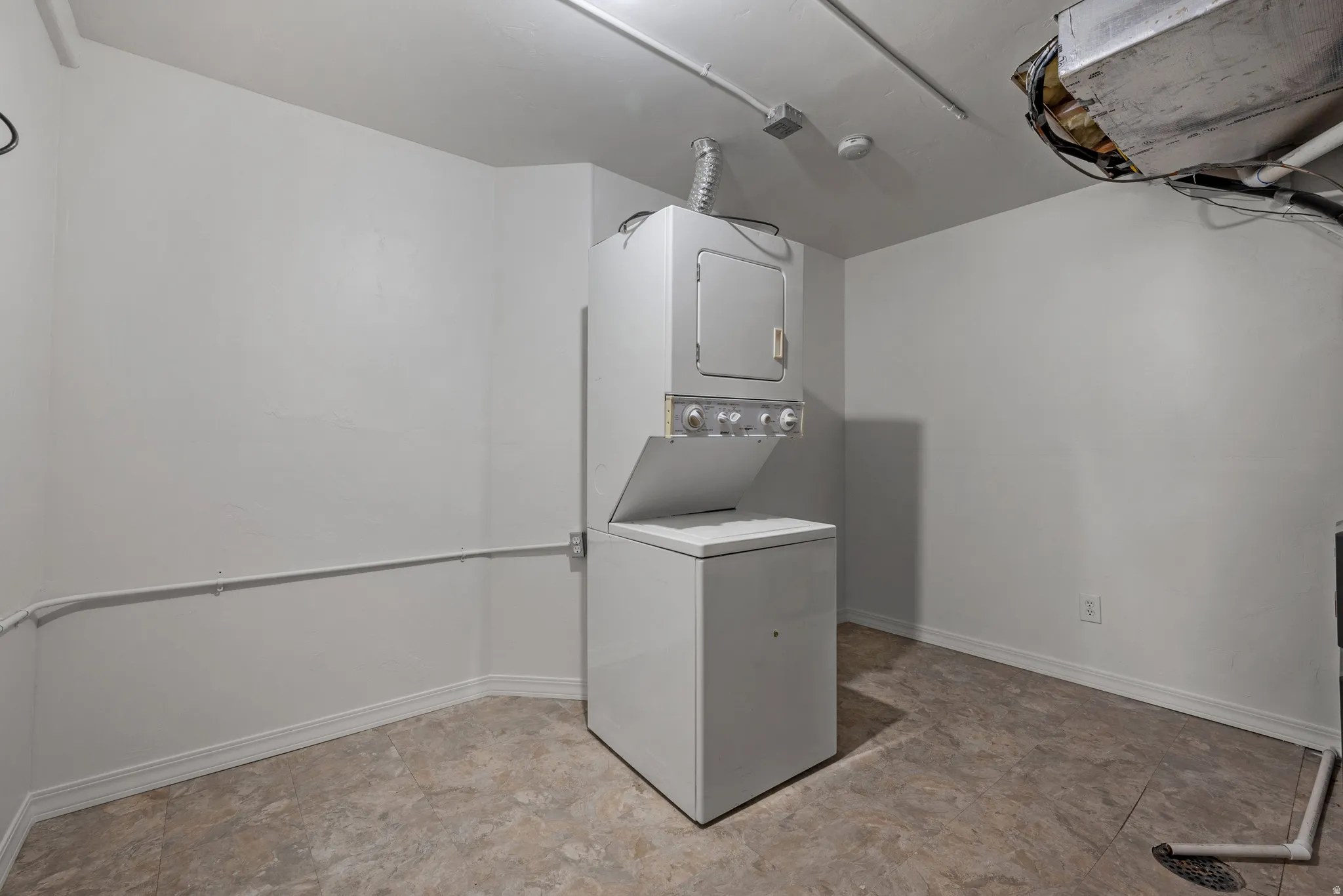 Dedicated laundry area with a white stacked washer and dryer unit, neutral-toned walls, and durable vinyl flooring