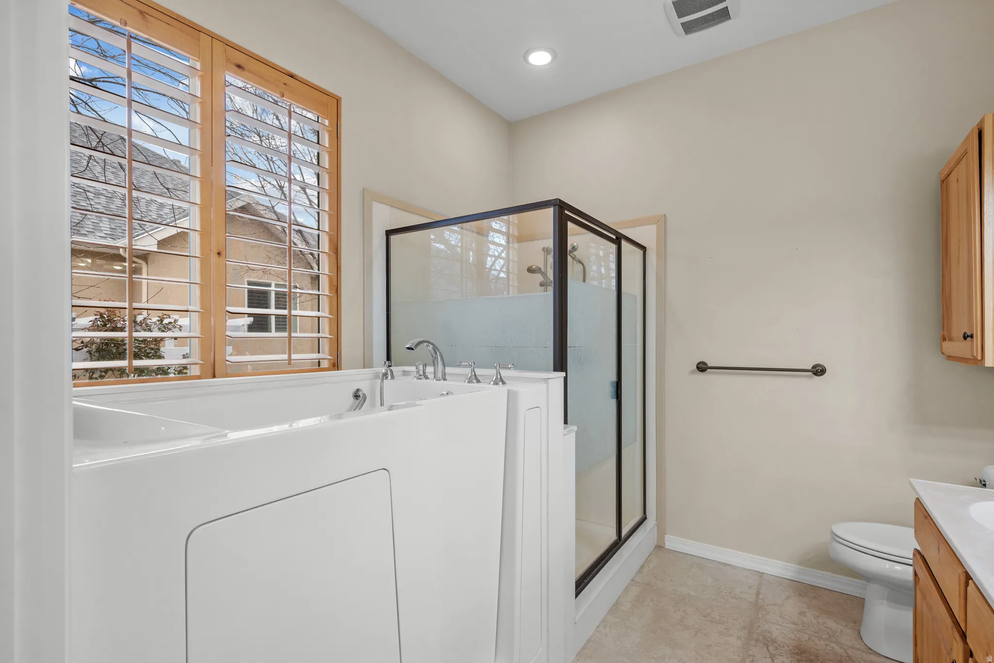 White walk-in bathtub with chrome fixtures, adjacent to a glass-enclosed shower with a frosted lower panel