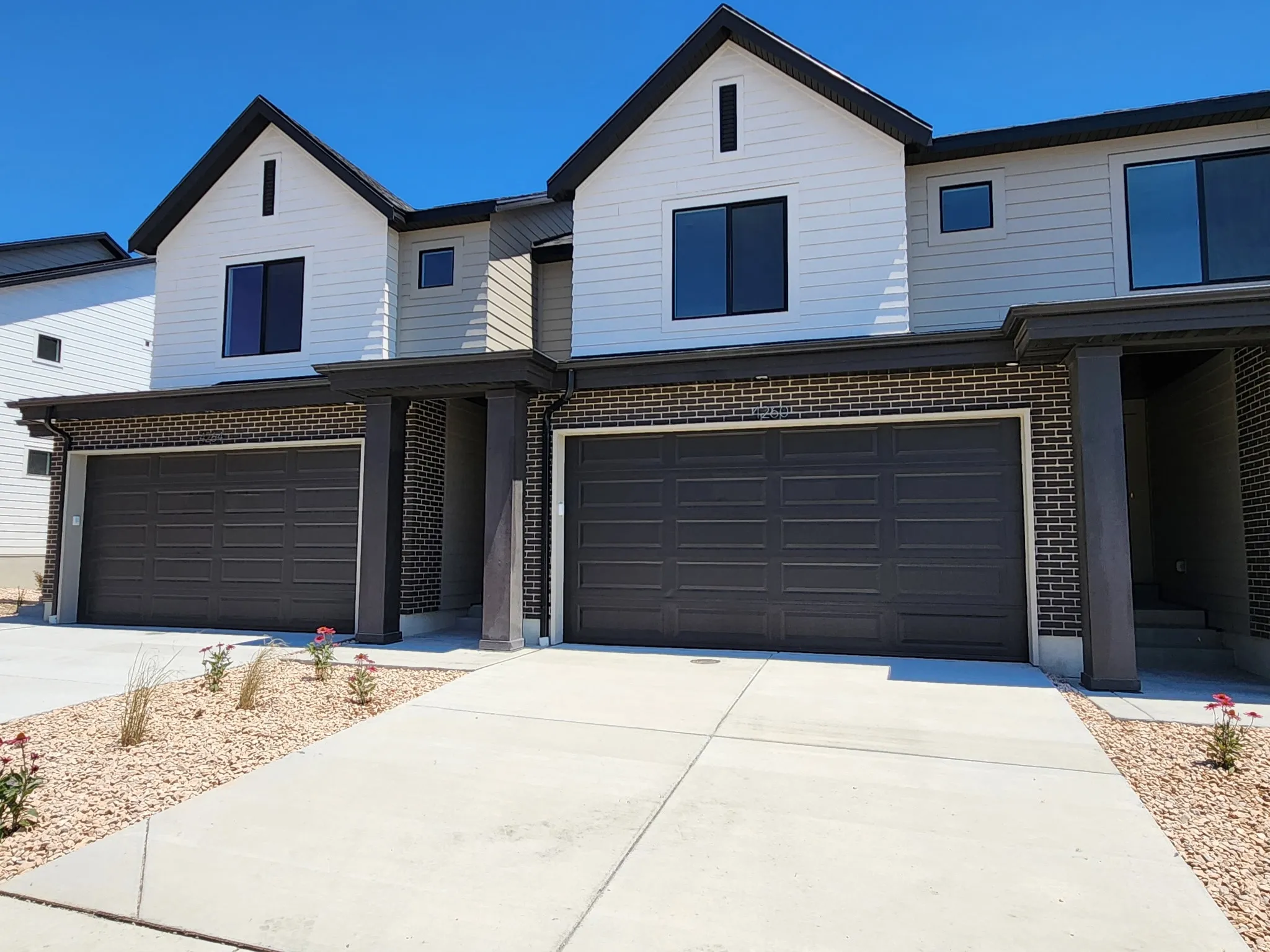 Contemporary townhome exterior featuring a two-car garage with panel doors, multi-tone brick accents, vertical siding, and dark-framed windows
