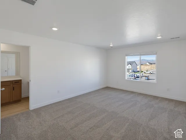 Carpeted flooring, recessed lighting, large window with blinds, wood-finish vanity with countertop, and wall-mounted mirror