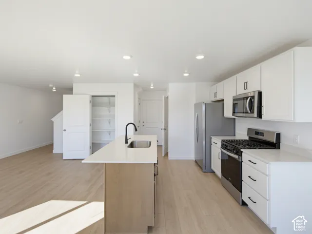 Modern kitchen featuring white cabinetry, stainless steel appliances, a center island with sink, quartz countertops, and wood-finish flooring