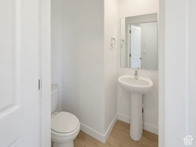 Pedestal sink with chrome faucet, wall-mounted mirror, and wood-finish flooring