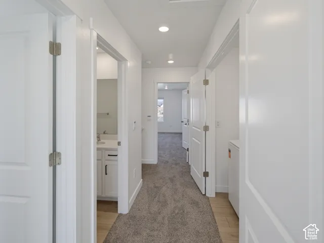 Hallway with recessed lighting, light-toned carpeting, wood-finish flooring, and white paneled doors