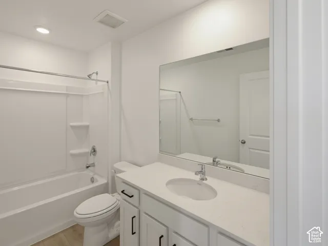 Bathroom featuring a white vanity with an undermount sink, a large wall-mounted mirror, wood-finish flooring, and a white bathtub with an integrated shower