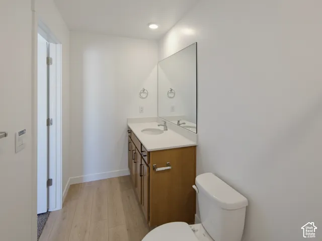 Wood-finish flooring, single vanity with light wood cabinetry, recessed lighting, wall-mounted mirror, and a toilet