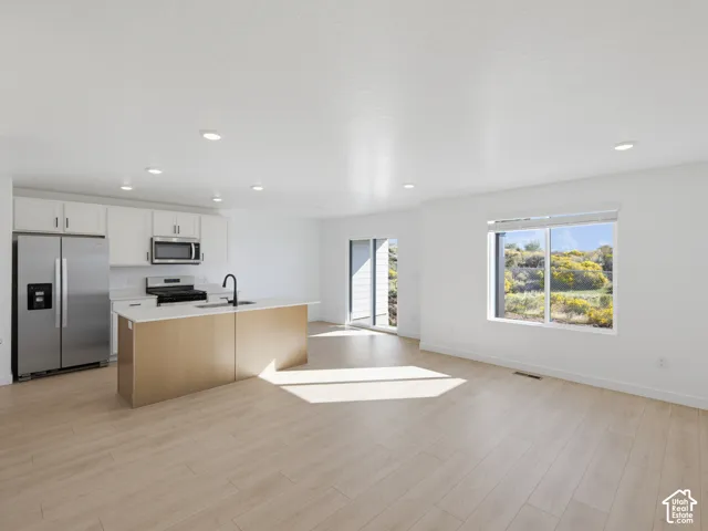 Open-concept living area featuring wood-finish flooring, recessed lighting, and a kitchen island with a built-in sink and a matte black faucet