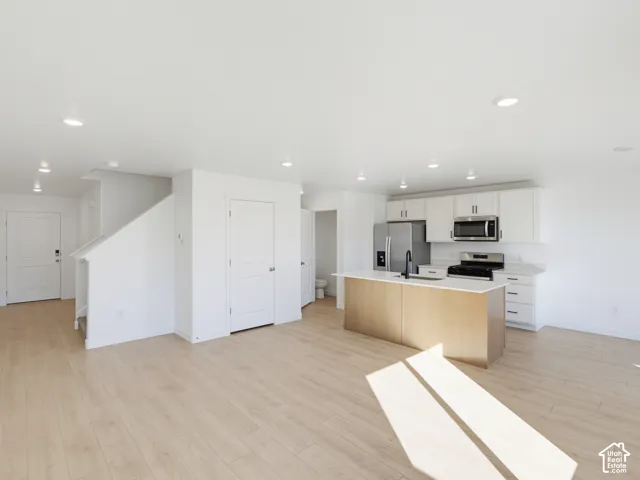 Contemporary kitchen featuring white cabinetry, stainless steel appliances, a center island with wood-finish paneling, and light wood-finish flooring