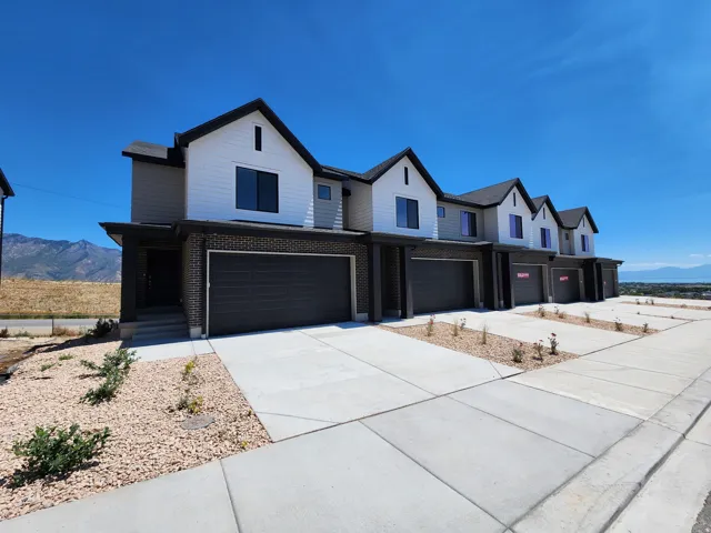 Modern townhome exterior with contrasting black and white siding, individual garage doors, paved driveways, and low-maintenance landscaping
