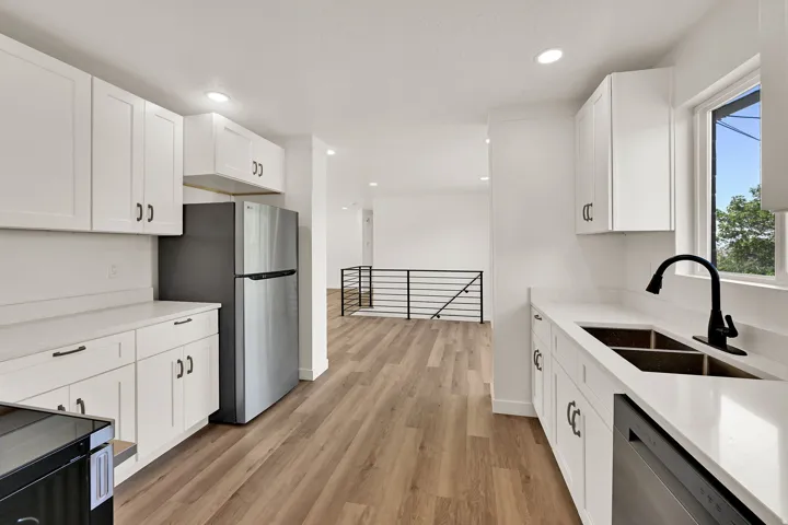 Modern kitchen featuring white cabinetry, light countertops, a stainless steel refrigerator, and wood-finish flooring