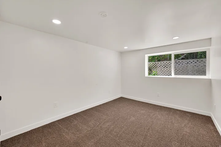 Carpeted room featuring white walls, recessed lighting, and a single window with a lattice-style security grating