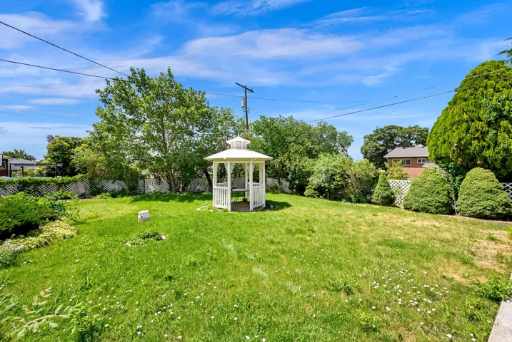 Spacious backyard featuring a white gazebo, mature trees, and a partial lattice fence