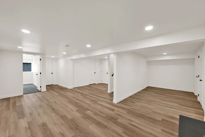 Spacious room featuring wood-finish flooring, recessed lighting, white walls, and multiple white doors with black hardware