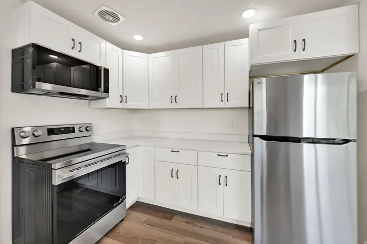 Kitchen featuring white shaker cabinetry, stainless steel appliances, light-toned countertops, and wood-finish flooring