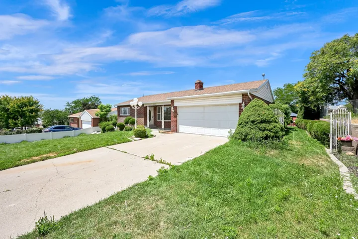 Brick facade residence featuring a two-car garage, concrete driveway, front porch, and mature landscaping