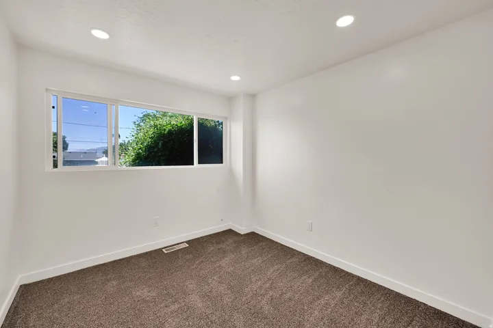 Bright interior space featuring a wide window, recessed ceiling lighting, clean white walls, white baseboards, and brown carpet flooring