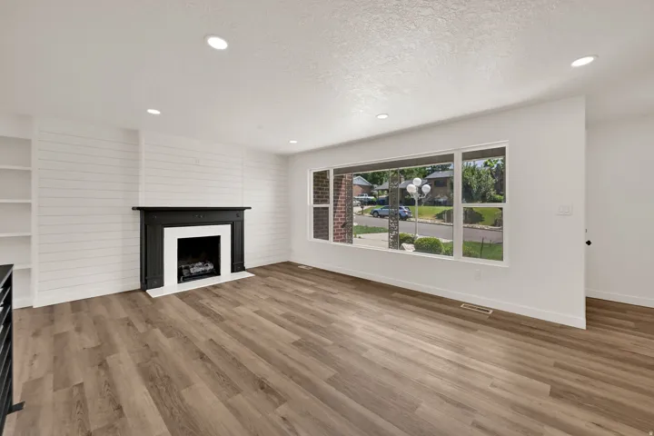 Living area featuring wood-finish flooring, a black mantle fireplace with white surround, recessed lighting, and a prominent shiplap accent wall