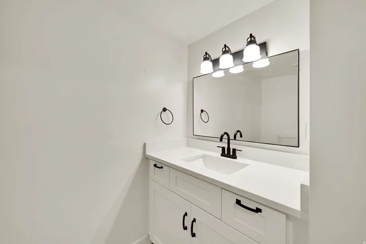 Bright white vanity with a white countertop and integrated sink, featuring a matte black faucet and coordinating mirror