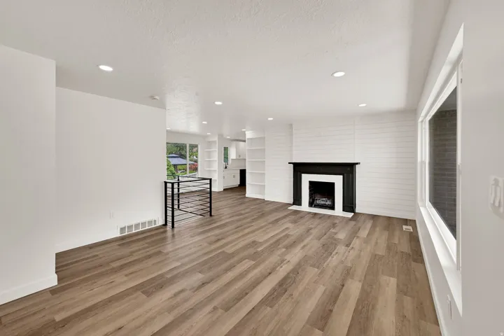 Spacious room featuring wood-finish flooring, recessed lighting, and a black fireplace with a white hearth