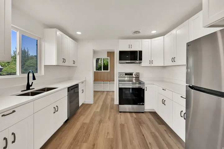 Modern kitchen featuring extensive white cabinetry, light-toned countertops, and wood-finish flooring