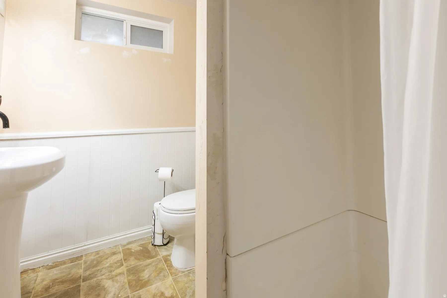 Bathroom featuring a white pedestal sink, toilet, and a window with frosted glass