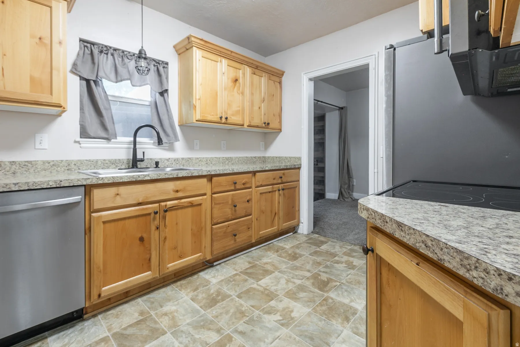 Kitchen featuring wood cabinetry, light-toned countertops, tile flooring, and a stainless steel dishwasher