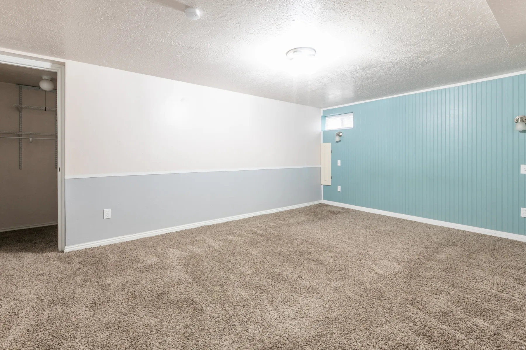 Carpeted room featuring a closet with wire shelving, two-tone walls with white and light gray, and a teal beadboard accent wall with sconce lighting