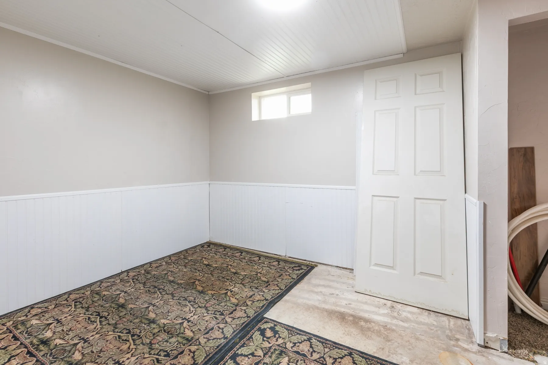 Interior room featuring light gray walls, white wainscoting, white paneled ceiling, and a high horizontal window