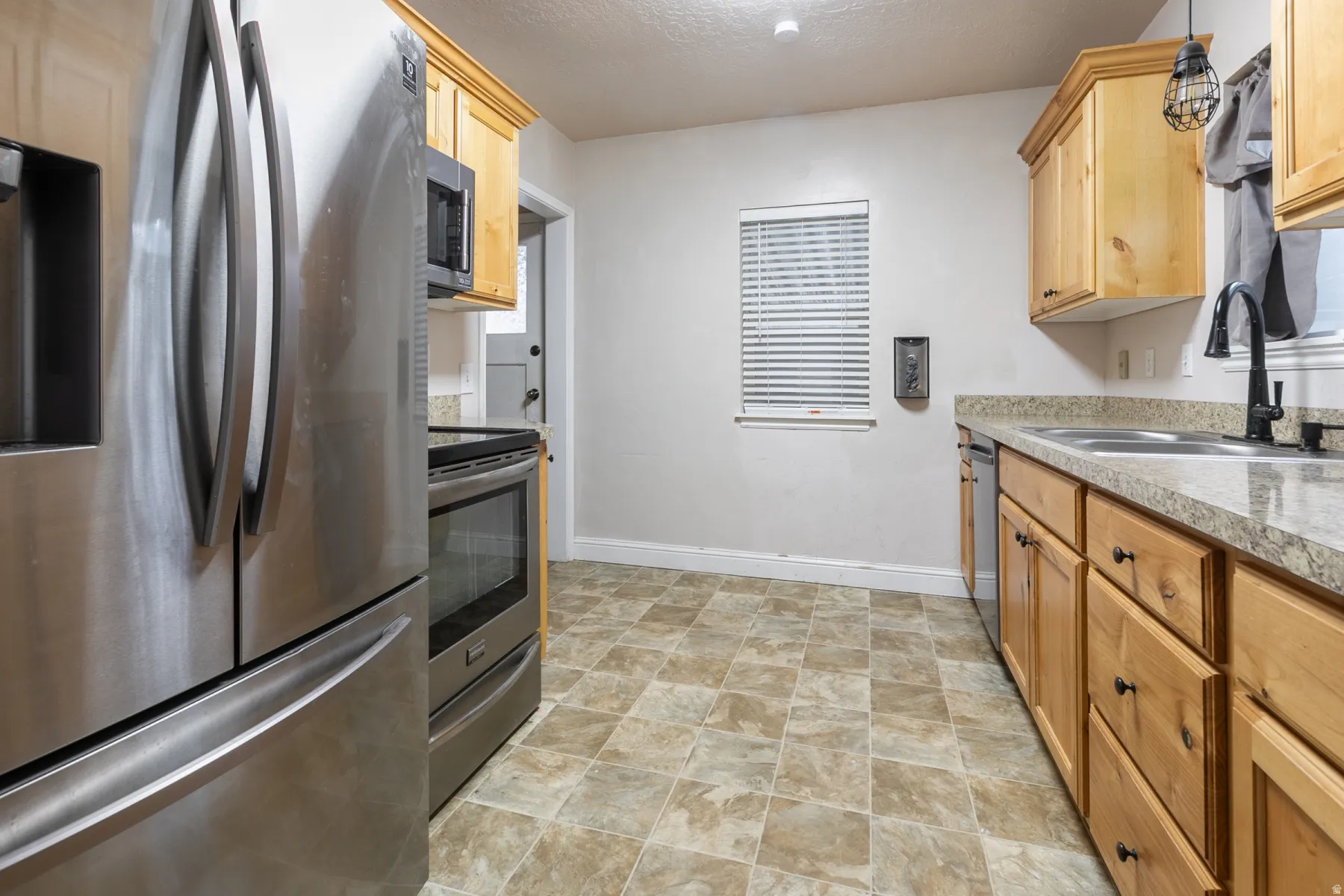 Kitchen featuring stainless steel appliances, light wood cabinetry, stone-finish countertops, and square tile flooring