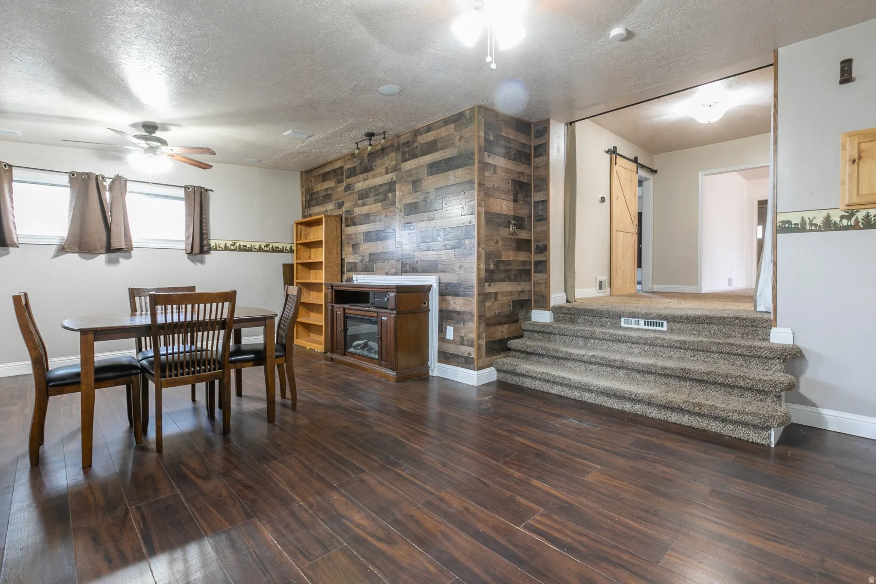 Spacious room featuring wood-finish flooring, a decorative accent wall, built-in electric fireplace, and recessed lighting