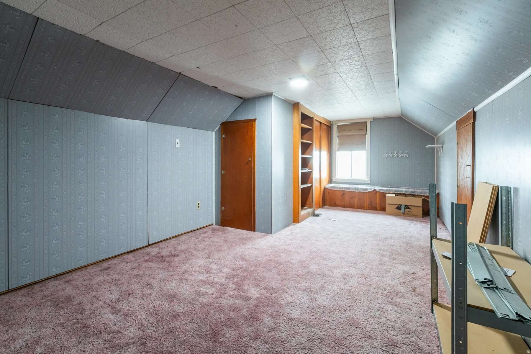 Spacious room featuring sloped ceilings, built-in shelving, a window with a built-in bench, and a flush-mount ceiling light