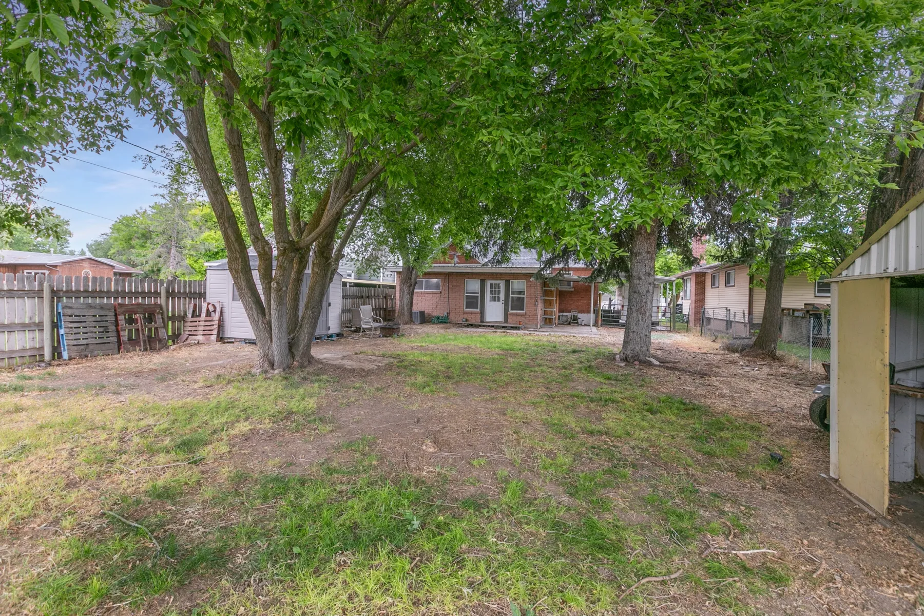 Expansive yard with mature trees, a detached storage shed, privacy fencing, and a brick exterior dwelling