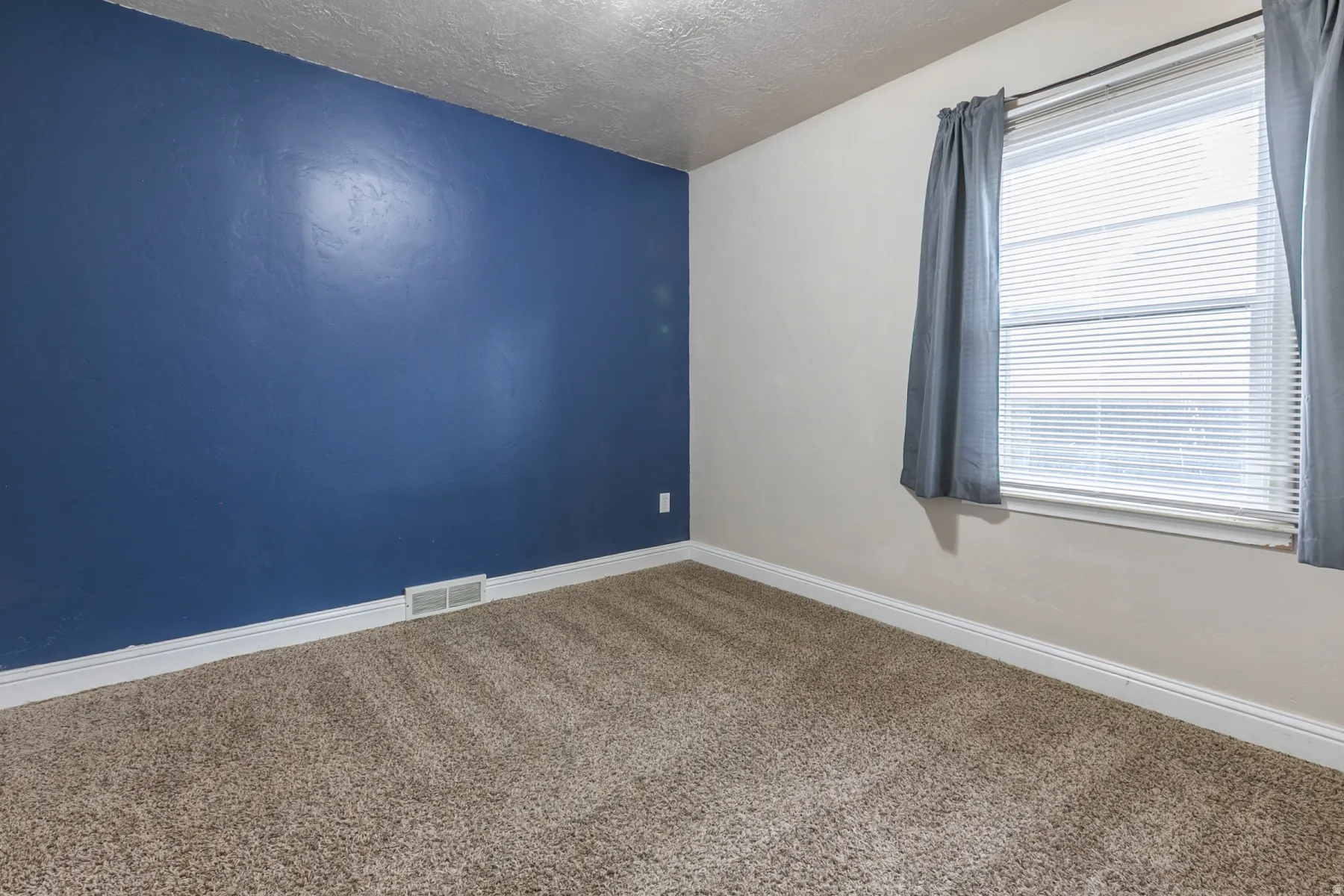 Carpeted room with a blue accent wall and a window featuring horizontal blinds