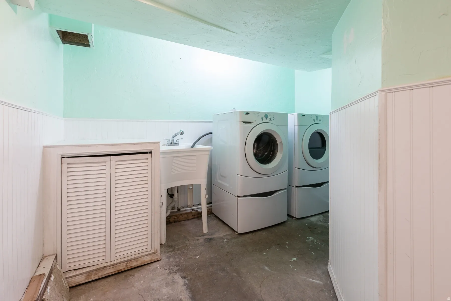 Laundry area featuring a utility sink, a pair of modern laundry units, white beadboard paneling, and a built-in louvered cabinet