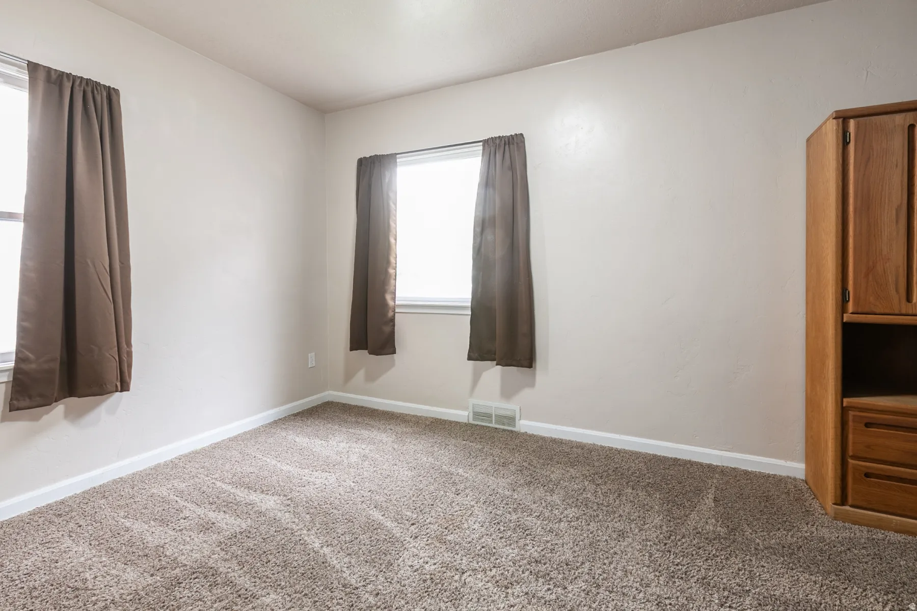 Carpeted room featuring two windows with valances and baseboard trim