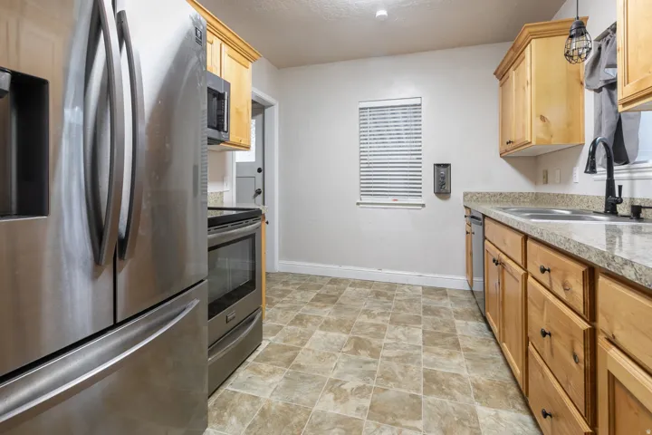 Kitchen featuring stainless steel appliances, light wood cabinetry, stone-finish countertops, and square tile flooring