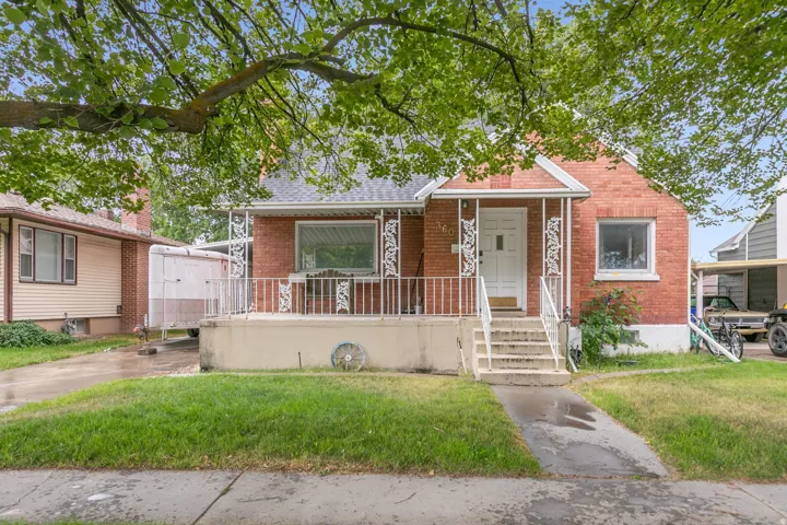 Red brick bungalow featuring a covered front porch with decorative white railing, a white entry door, an asphalt shingle roof, and a concrete pathway