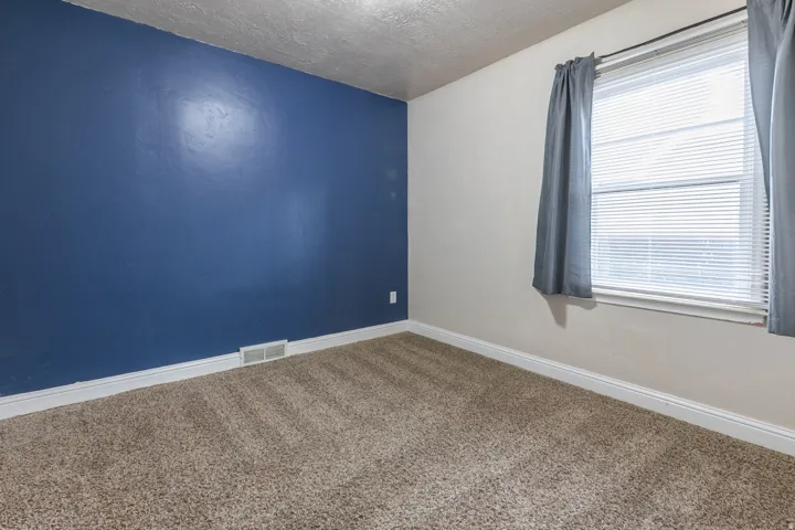 Carpeted room with a blue accent wall and a window featuring horizontal blinds