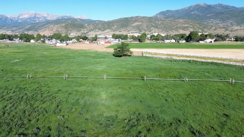 Expansive green field featuring an irrigation system, bordered by a white fence and a distant community, with mountains forming a backdrop