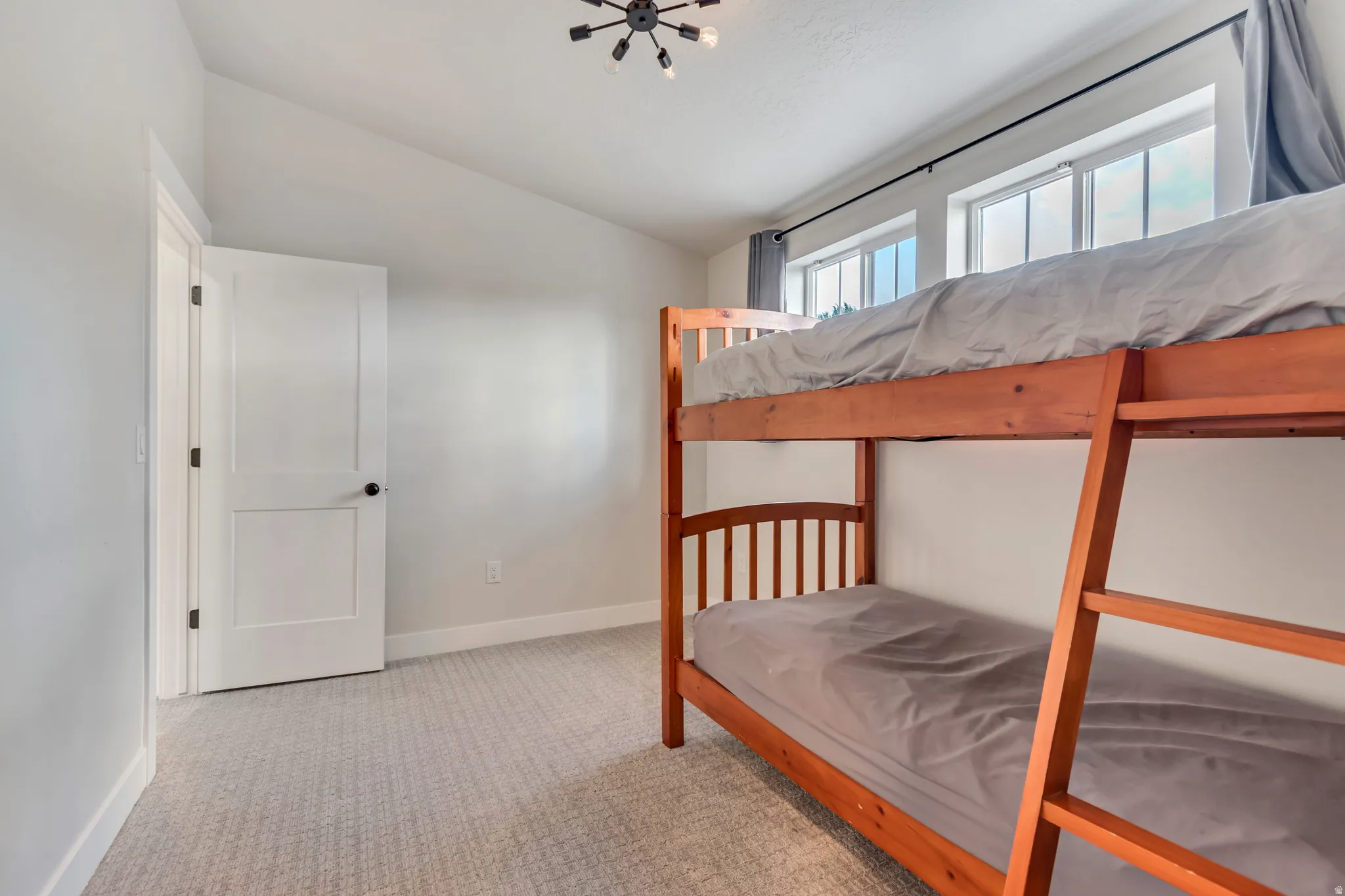 Bright room featuring abundant natural light from multiple windows, vaulted ceiling, neutral wall paint, white trim, and patterned carpet flooring
