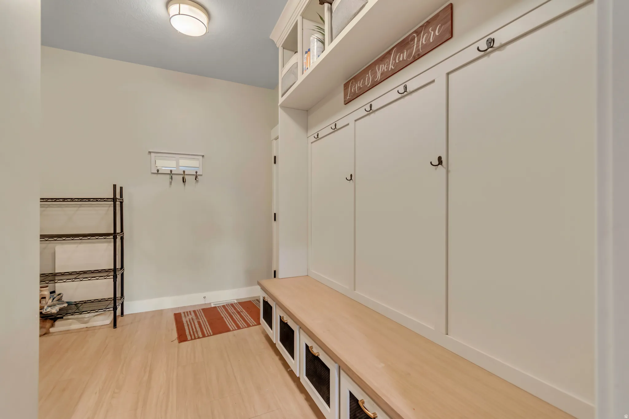 Built-in mudroom storage featuring a long wood bench, individual cabinet compartments with matte black hooks, and upper open shelving