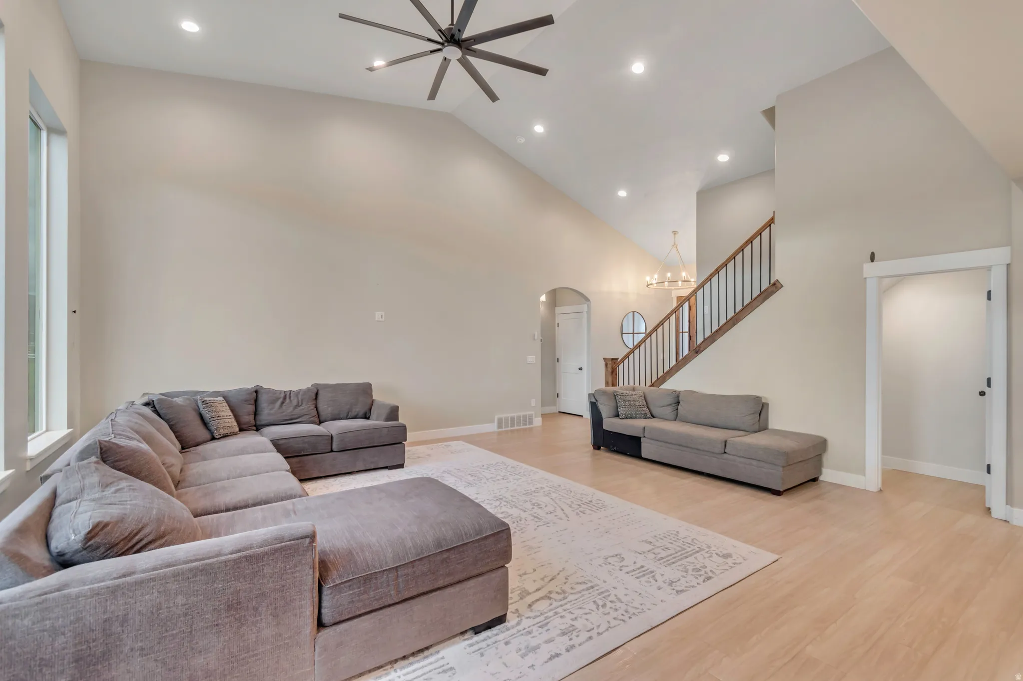Living area featuring vaulted ceilings, recessed lighting, wood-finish flooring, and a staircase with wood handrails and black balusters