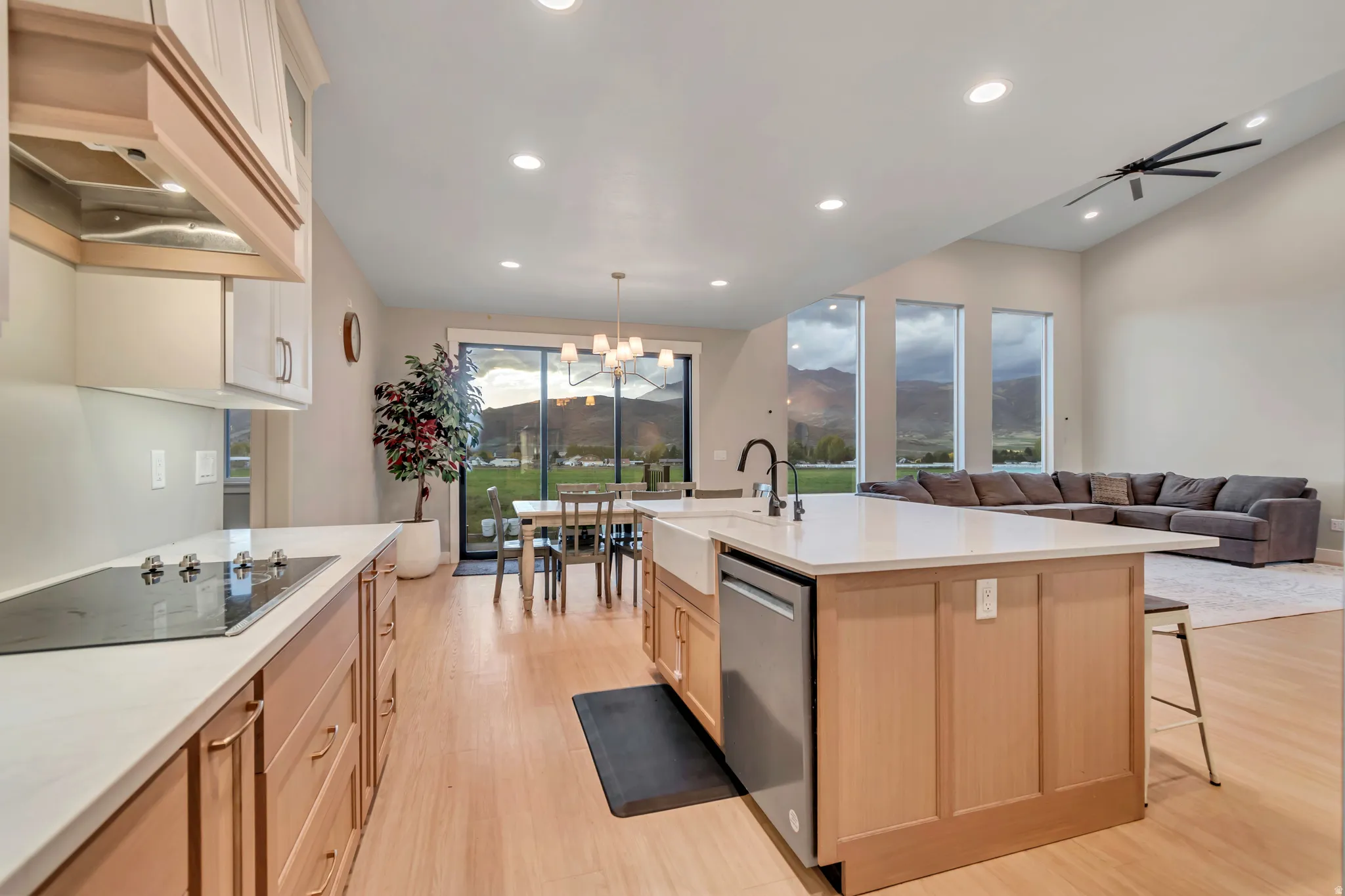 Open-concept kitchen featuring light wood-finish cabinetry, a large center island with a farmhouse sink, and a cooktop range