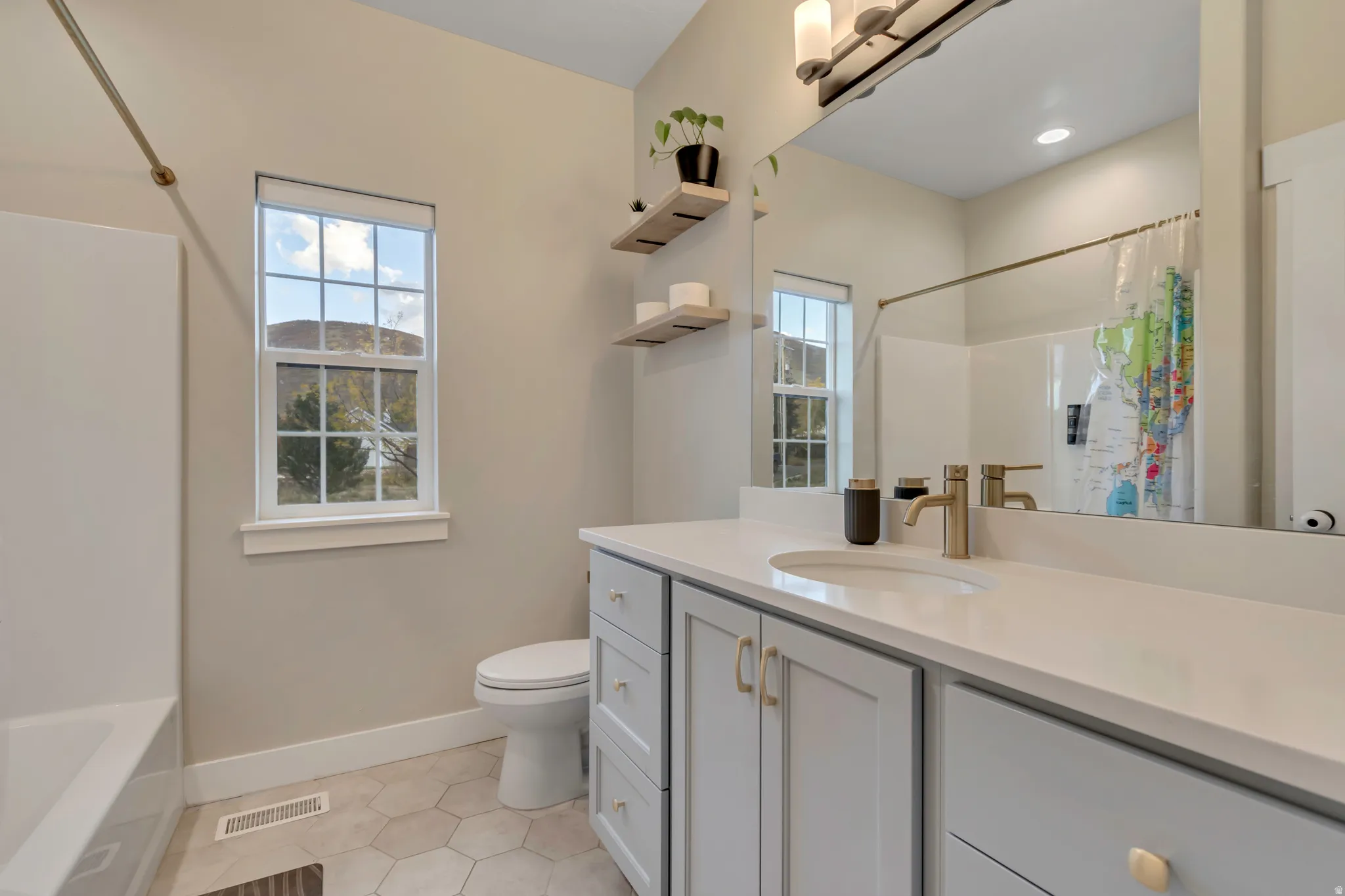 Bathroom featuring a single vanity with light grey cabinetry, white countertop, and gold-finish hardware