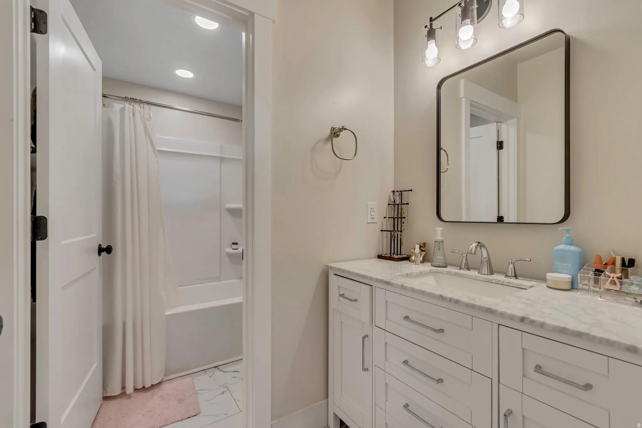Bathroom vanity featuring a single undermount sink, a stone countertop, and white shaker-style cabinetry with chrome hardware