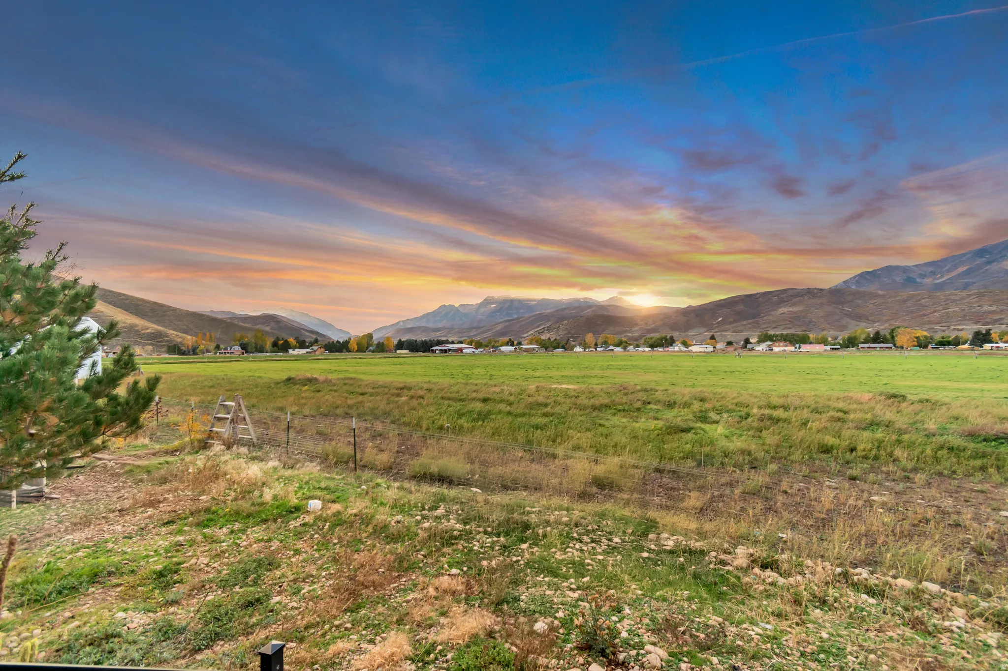 Expansive green fields framed by distant mountains and a vibrant sunset sky