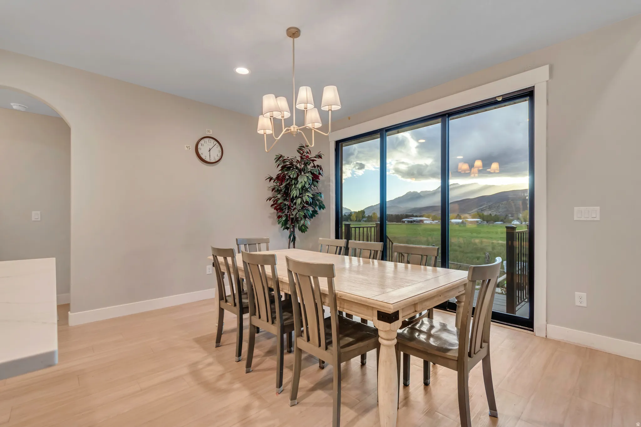 Spacious dining area featuring wood-finish flooring, a contemporary chandelier, an arched doorway, and expansive sliding glass doors opening to a scenic mountain and field backdrop