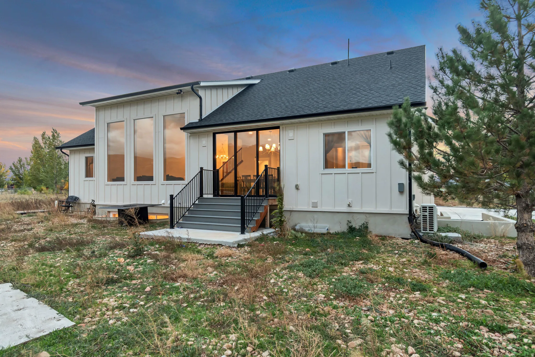 Modern farmhouse exterior with white board and batten siding, a dark shingle roof, and a prominent dark-railed staircase leading to a glass sliding door